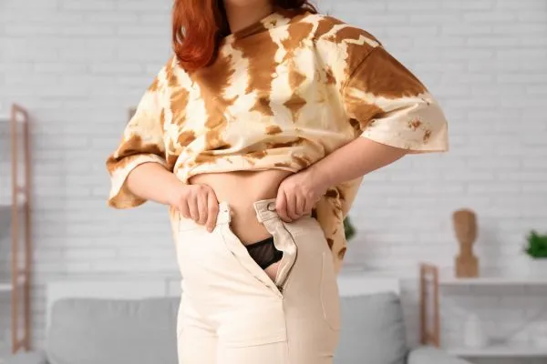 Image of woman trying to do her trousers up after pregnancy weight gain Dorking